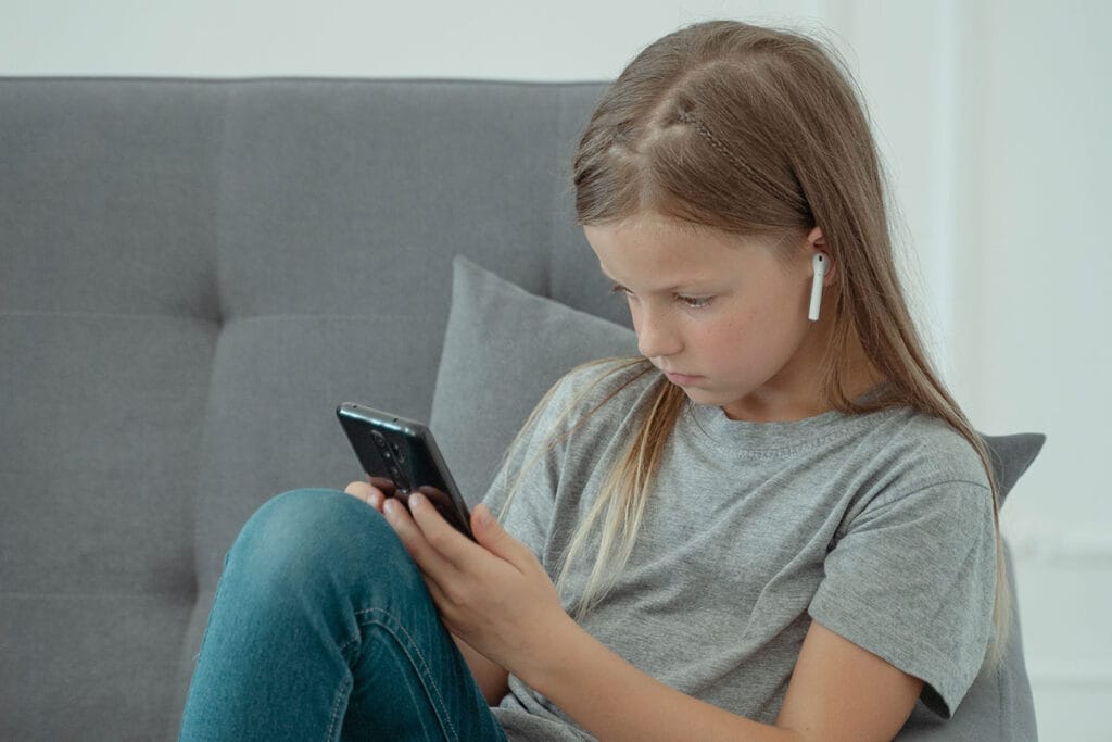 girl sitting on the couch using mobile phone and wireless earphones